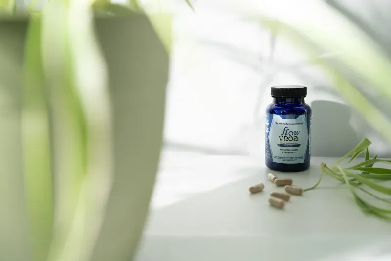 FlowVeda bottle on a white surface with a spider plant and loose capsules.