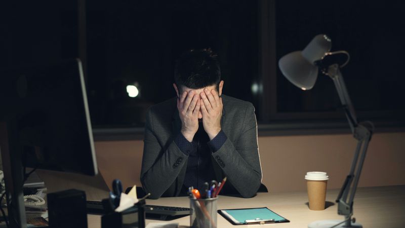 A man at a dark desk with his face in his hands.