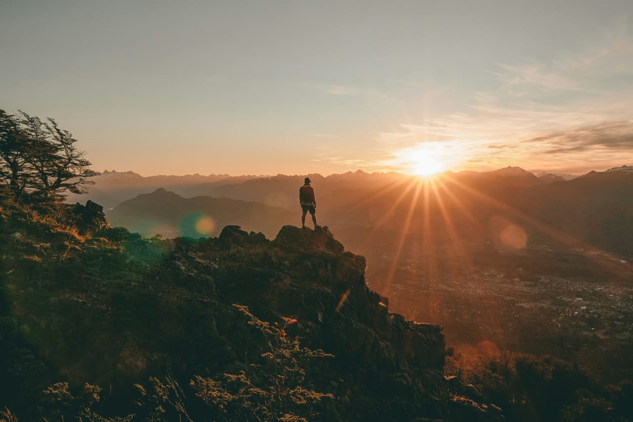 A lone figure on a mountain summit at sunrise overlooking a vast range